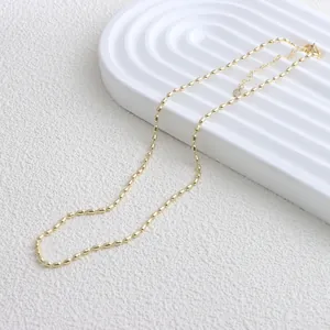Detailaufnahme einer minimalistischen goldenen Reiskorn-Kette auf weißem Dekor.