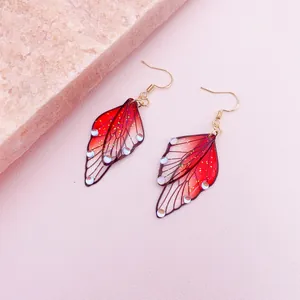 Close-up detail of red gradient butterfly wing earrings with glitter and crystal gems.