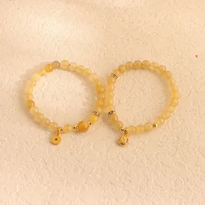 Nahaufnahme von zwei gelben Citrin-Perlenarmbändern mit goldenen Münzen und Buddha-Anhang