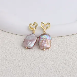 Dettaglio di eleganti orecchini a perno con perle barocche viola e cuori dorati.