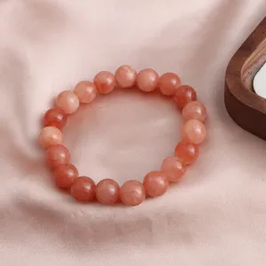 Nahaufnahme eines Sonnenstein Kristall Armbands auf elegantem rosa Seidenstoff Hintergrund.
