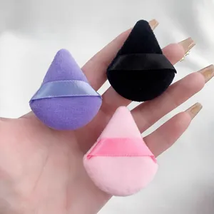 Detailopname van mini driehoekige make-up poederdonsjes in paars, zwart en roze.