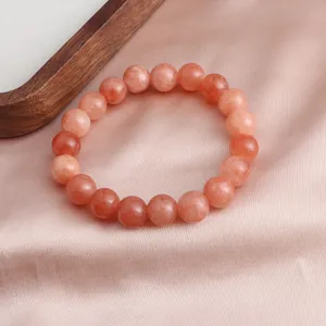 Nahaufnahme eines orangefarbenen Sonnenstein-Armbands auf rosa Satinhintergrund.