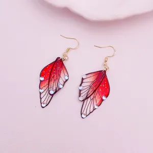 Close-up of red gradient butterfly wing earrings with gold hooks and glitter details.