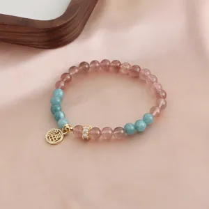Detailed view of a strawberry crystal bracelet with a gold Fu fortune charm.