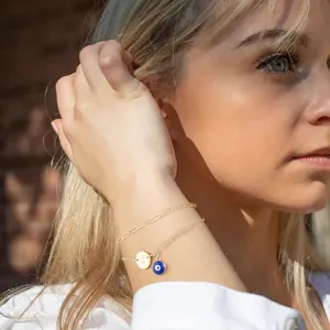 Detailed view of a gold double-layer bracelet with J-letter charm and blue evil eye.
