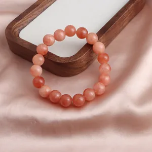 Nahaufnahme eines natürlichen Sonnenstein-Armbands auf elegantem rosa Seidenhintergrund