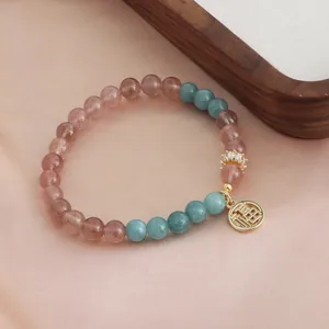 Detailed view of a natural strawberry quartz and turquoise crystal bracelet with gold Fu charm.