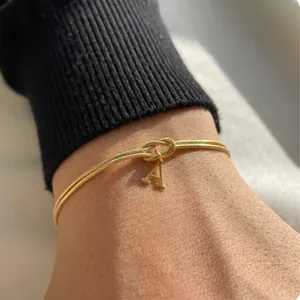 Close-up of gold-plated snake chain bracelet with a knotted initial A pendant on a wrist.