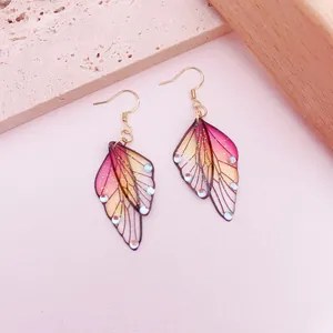 Close-up of translucent pink and yellow butterfly wing earrings with glitter detail