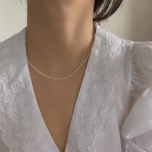 Detailansicht einer zarten Saatperlenkette am Hals mit einer weißen Spitzenbluse