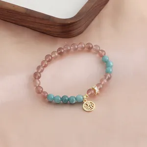 Detailed macro shot of natural strawberry quartz bracelet with golden 'Fu' blessing charm