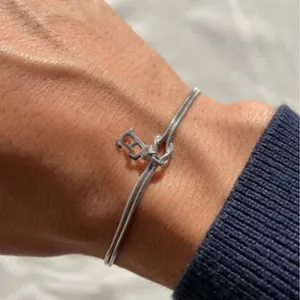 Detail of a knotted snake chain bracelet with a metallic initial E charm on a wearer's wrist.