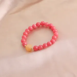 Nahaufnahme eines rosa Kristallarmbands mit Kürbis-Anhänger auf edler Seide liegend.