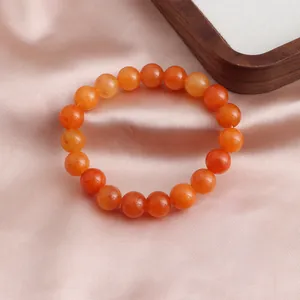Detailansicht eines runden orangefarbenen Sonnenstein-Armbands auf rosa Seidenstoff