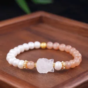 Close-up detail of natural white jade and sunstone beaded bracelet with carved cat charm