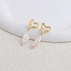 Dettaglio ravvicinato di orecchini a cuore dorati con eleganti perle barocche.