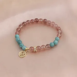 Close-up of natural strawberry quartz bracelet with a gold luck pendant and silk background.