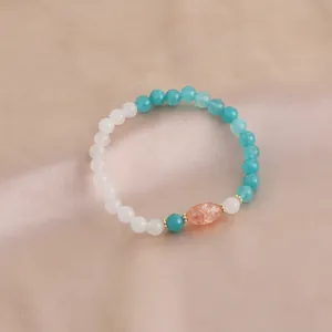 Detail eines Naturkristall-Armbands mit blauen und weißen Perlen und orangem Stein.
