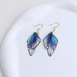 Detail of blue and purple butterfly wing earrings with iridescent rhinestones and gold hooks.