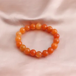 Nahaufnahme eines leuchtend orangefarbenen Sonnenstein-Perlenarmbandes auf Satin