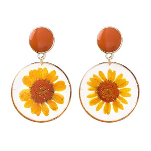 Dettaglio degli orecchini in resina fatti a mano con veri fiori di margherita gialla essiccati.