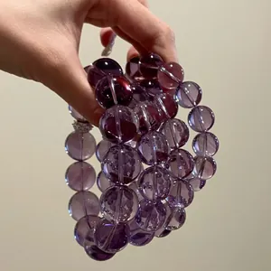 Detailed close-up of a 12mm natural purple amethyst bead bracelet held by a fair hand.