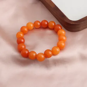 Detailansicht eines orangefarbenen Sonnenstein-Perlenarmbands auf rosa Seidenhintergrund