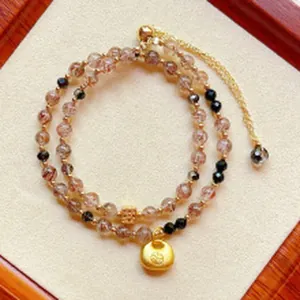 Close-up detail of a double-layer rutilated quartz beaded bracelet with a gold pendant