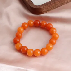 Nahaufnahme eines leuchtend orangefarbenen Sonnenstein-Armbands auf rosa Seidenstoff.