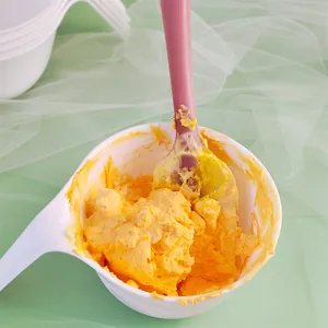 Close-up of pink silicone spatula mixing yellow buttercream frosting in a white bowl