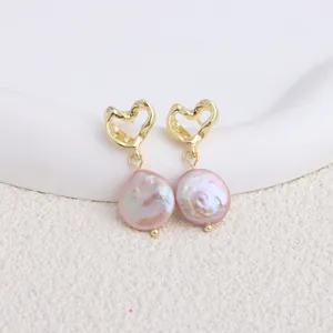 Dettaglio orecchini a cuore dorati con perle barocche rosa su sfondo bianco pulito