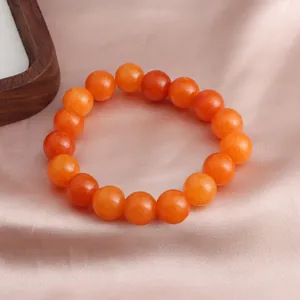 Nahaufnahme eines leuchtend orangefarbenen Sonnenstein-Armbands auf rosa Satinstoff-Hintergrund