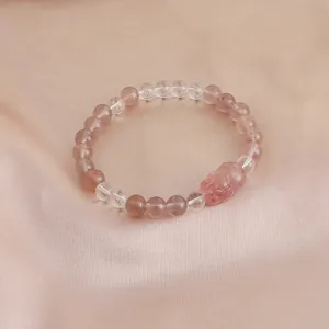 Detail view of strawberry quartz bracelet with cute carved pig charm on pink satin
