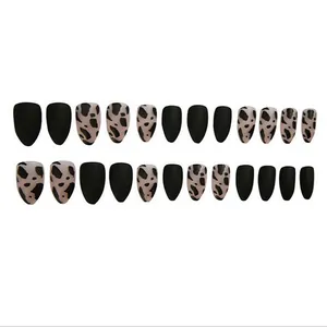 Detailed macro view of matte black and cow print almond-shaped press-on nail set.