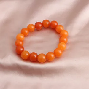 Makroaufnahme eines leuchtend orangefarbenen Sonnenstein-Perlenarmbands auf Seidenstoff