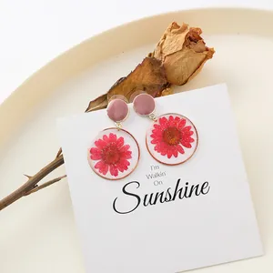 Dettaglio di orecchini tondi con veri fiori di crisantemo rosso essiccati in resina trasparente