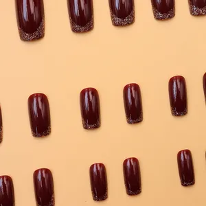 Close-up detail of glossy burgundy press-on nails featuring elegant gold glitter gradient tips.
