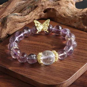 Macro detail of natural amethyst beaded bracelet with golden butterfly charm on wooden stand