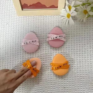 Four teardrop-shaped makeup cushion puffs in pink and orange colors with ribbons