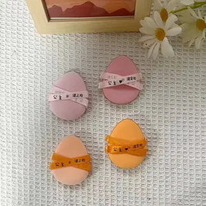 Macro view of four teardrop-shaped makeup puffs in pink and orange with decorative ribbons