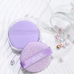 Close-up detail of a soft purple double-sided makeup powder puff with ribbon handle and case