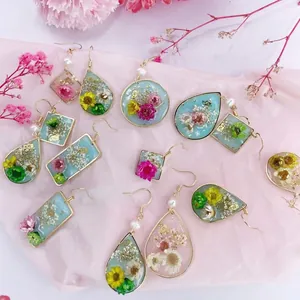 Vista detallada de varios pendientes geométricos de resina con flores secas reales