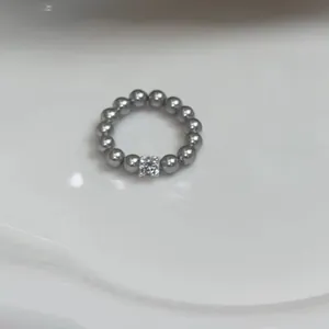 Detail van een grijze parelring met een vierkante kristal in het midden op wit
