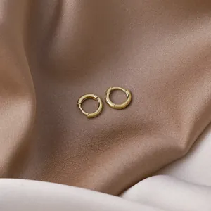 Detailed macro view of minimalist small gold hoop earrings on soft champagne silk background