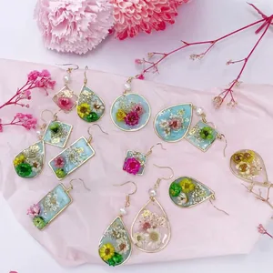 Pendientes de resina hechos a mano con flores secas reales y detalles en pan de oro elegantes.