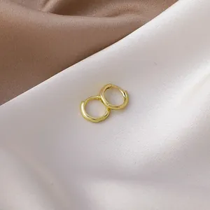 Small minimalist gold-plated huggie hoop earrings on soft silk fabric background