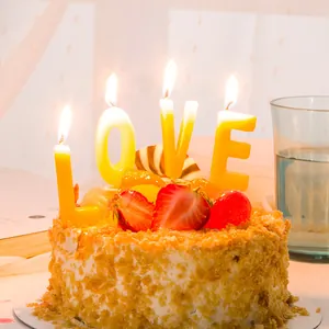 Velas creativas amarillas con letras LOVE encendidas en un pastel de fresas para cumple
