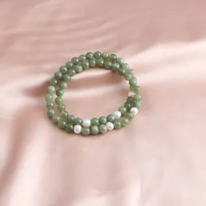 Macro view of double-layered green jade and white pearl beaded bracelet on pink satin