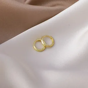 Close-up of minimalist gold-plated small huggie hoop earrings on silk fabric